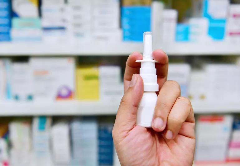 Hand holding nasel spray product with store shelves of medicine in the background.