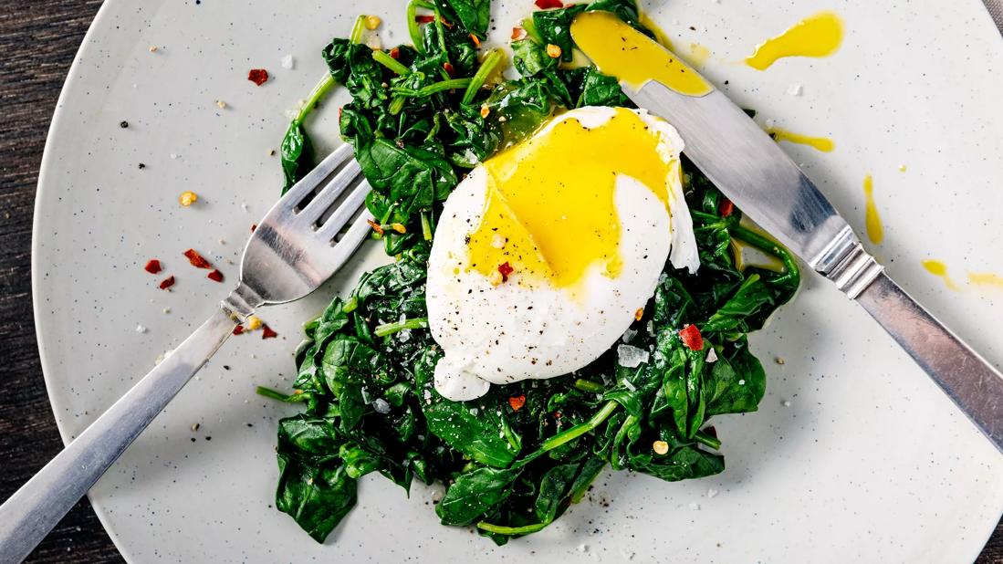 Poached egg on bed of spinach with red pepper, with fork and knife on plate