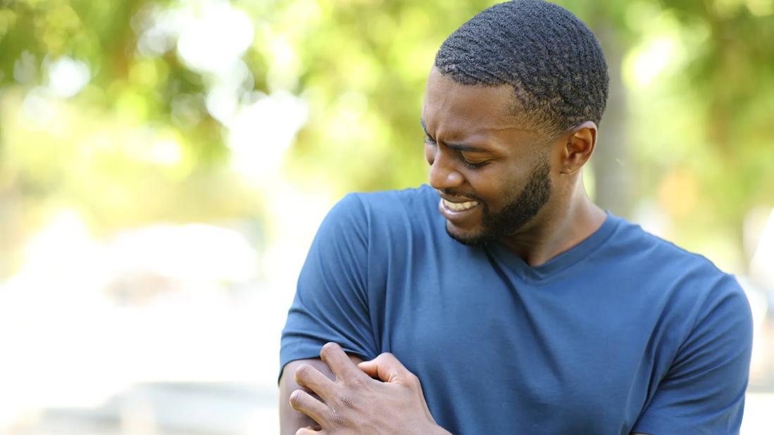 Person grimacing while scratching an itch on their arm