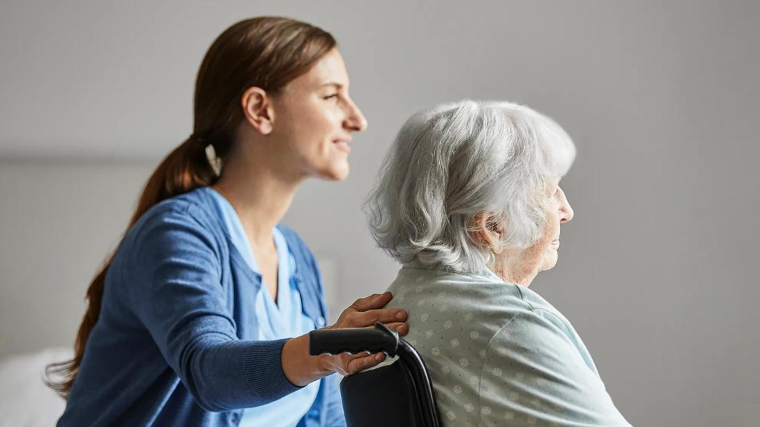 female caregiver with hand on back of elderly woman in wheelchair