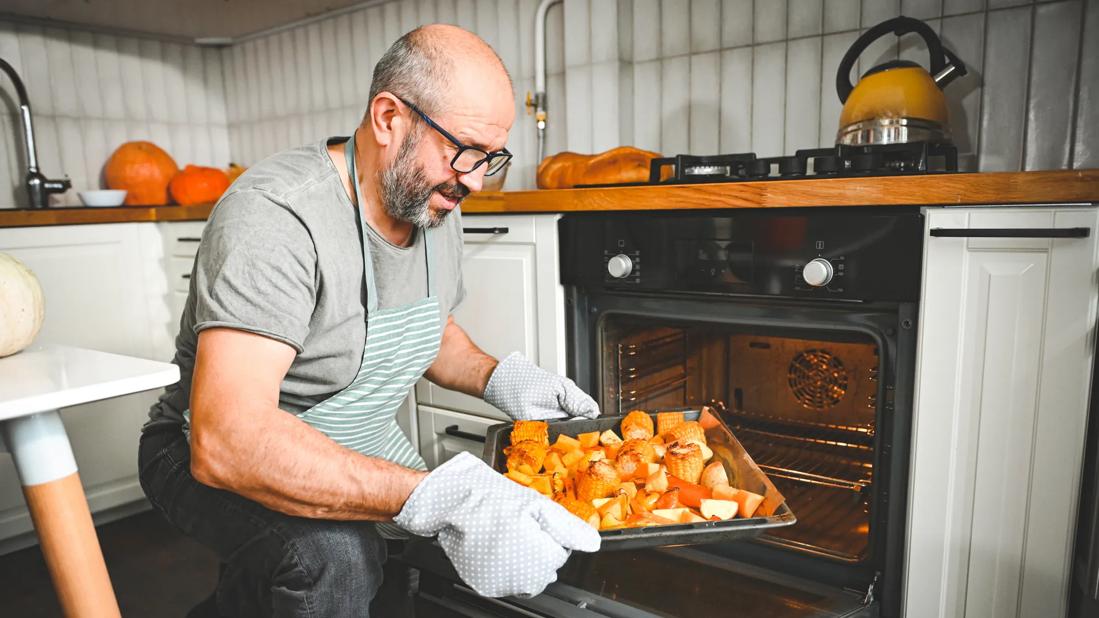 Person wearing oven mitts removing a baking sheet of vegetables from the oven