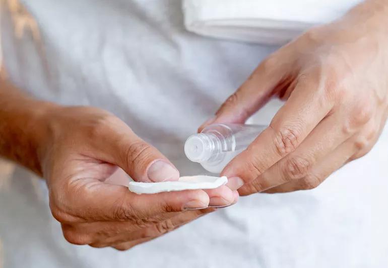 Person applying skin toner to cotton pad before using it on their face.