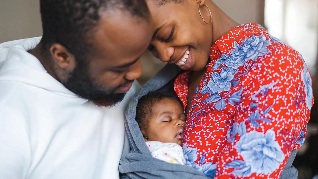 Smiling new parents holding swaddled newborn baby