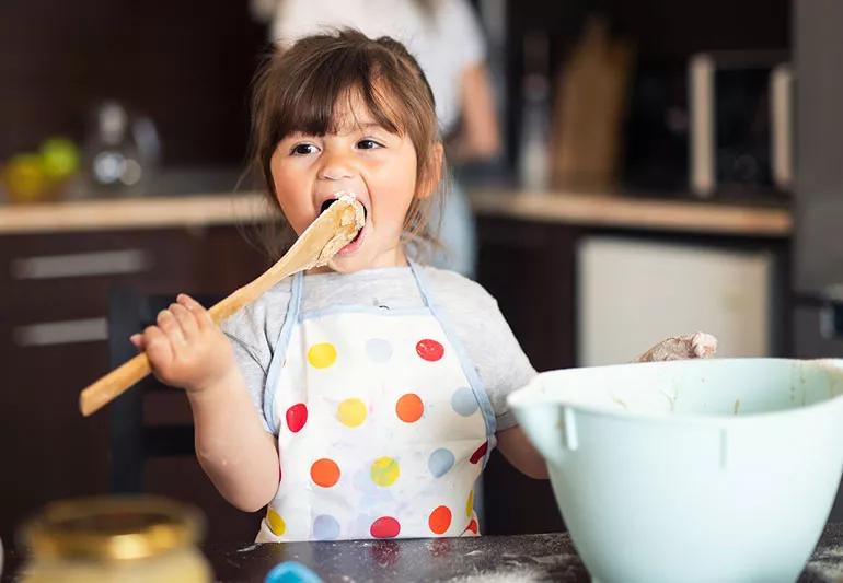 Girl eating cookie dough while cooking with mom