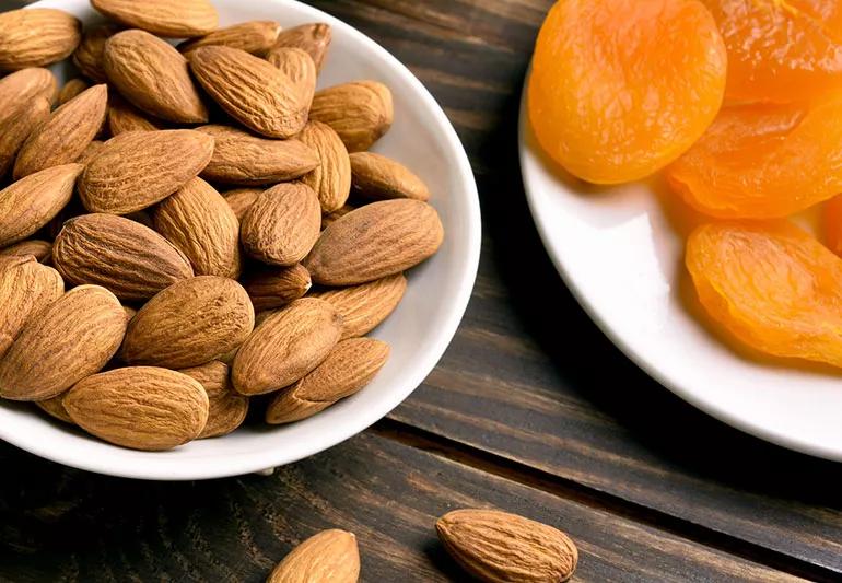 Bowl of almonds and plate of dried apricots.