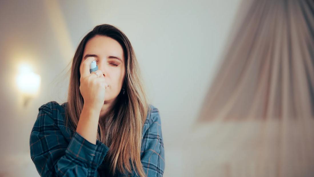 Person with eyes closed, inhaling on an asthma inhaler