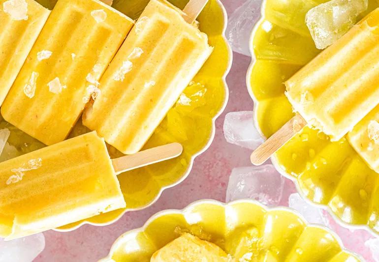An assortment of bright yellow, frozen tropical fruit pops are displayed in yellow bowls.