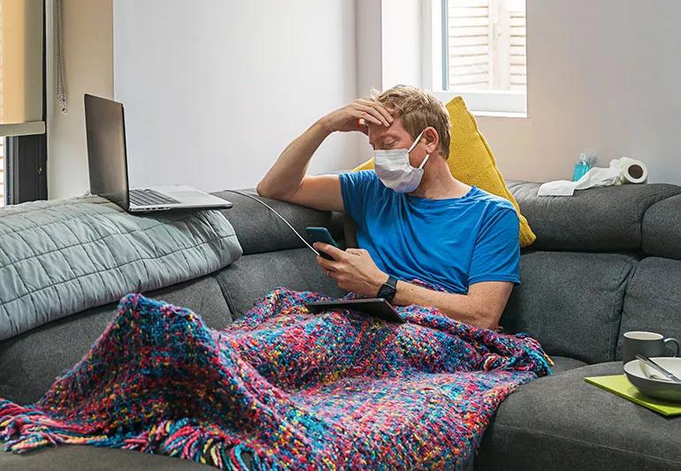 man with coronavirus holding head while on couch at home