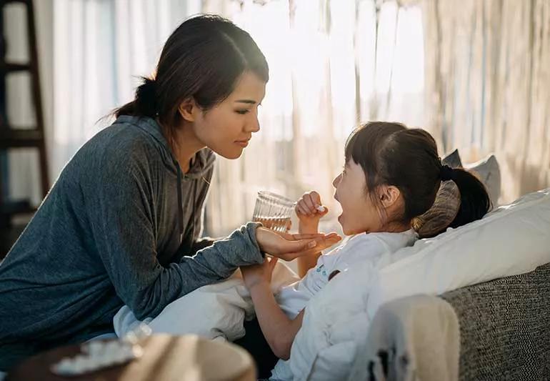 Mother giving child medicine to take with water.