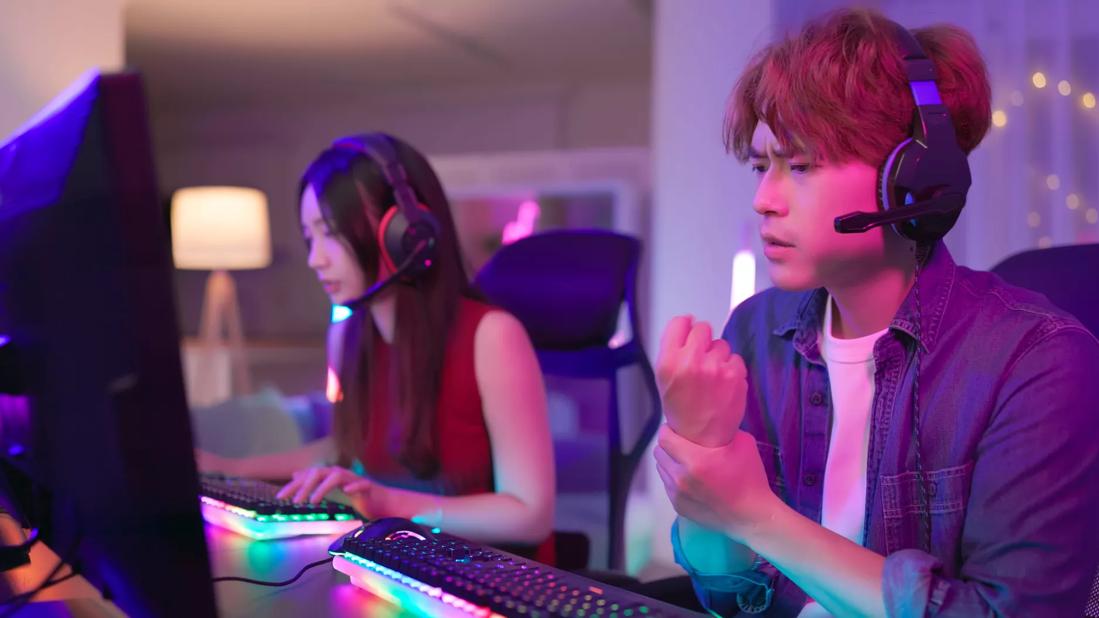 Asian male rubbing wrist while playing video game