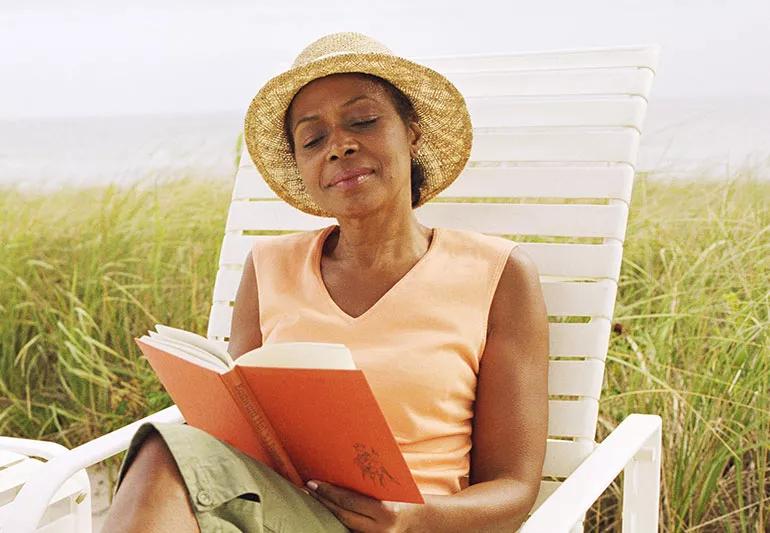 Person reading at beach wearing sunhat.