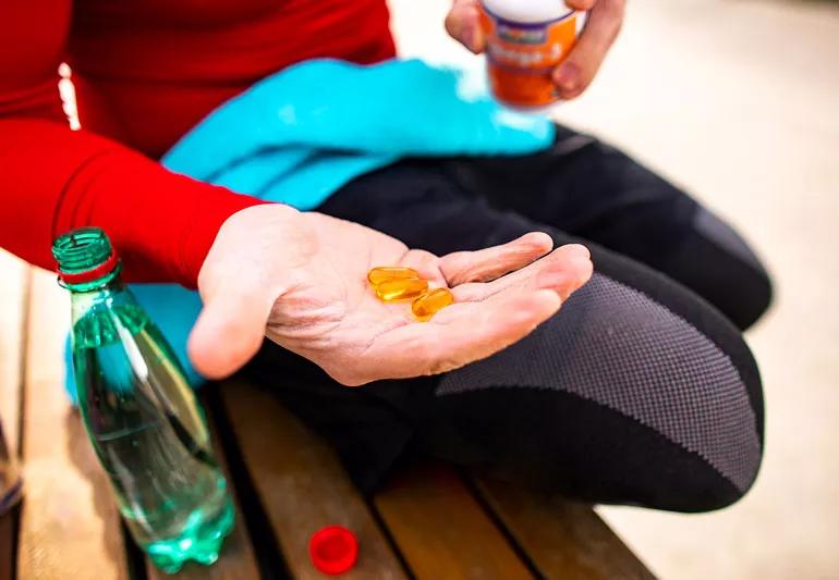 Close up photo of a person holding three orange pills in their hand