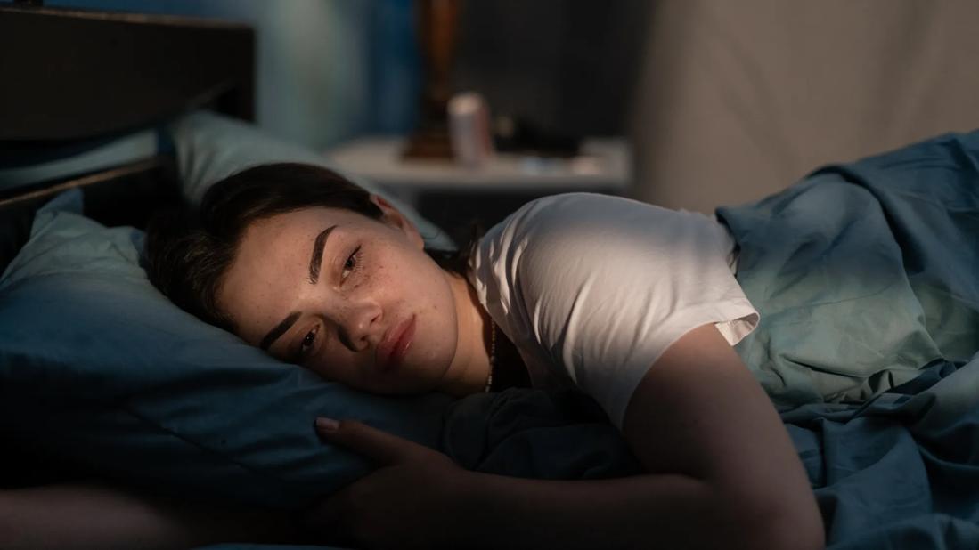 Person lying in bed on their side at night with their eyes open