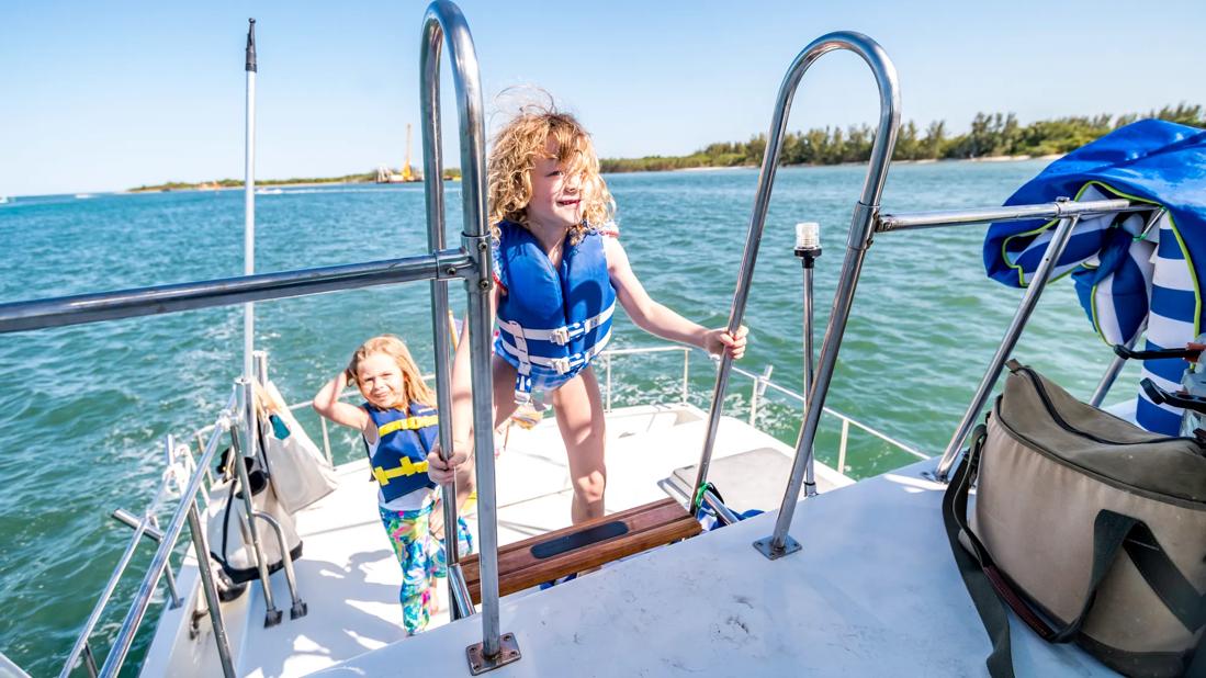 Two happy kids in lifejackets climbing ladder to top deck of boat