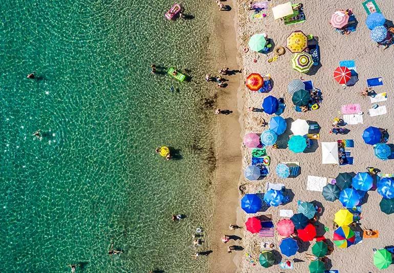 Aerial view of ocean with beach umbrellas and people swimming.