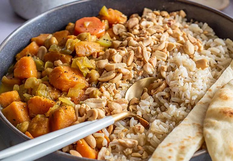 Vegetable massamam in a skillet with carrots, onion, chickpeas, rice and peanuts.