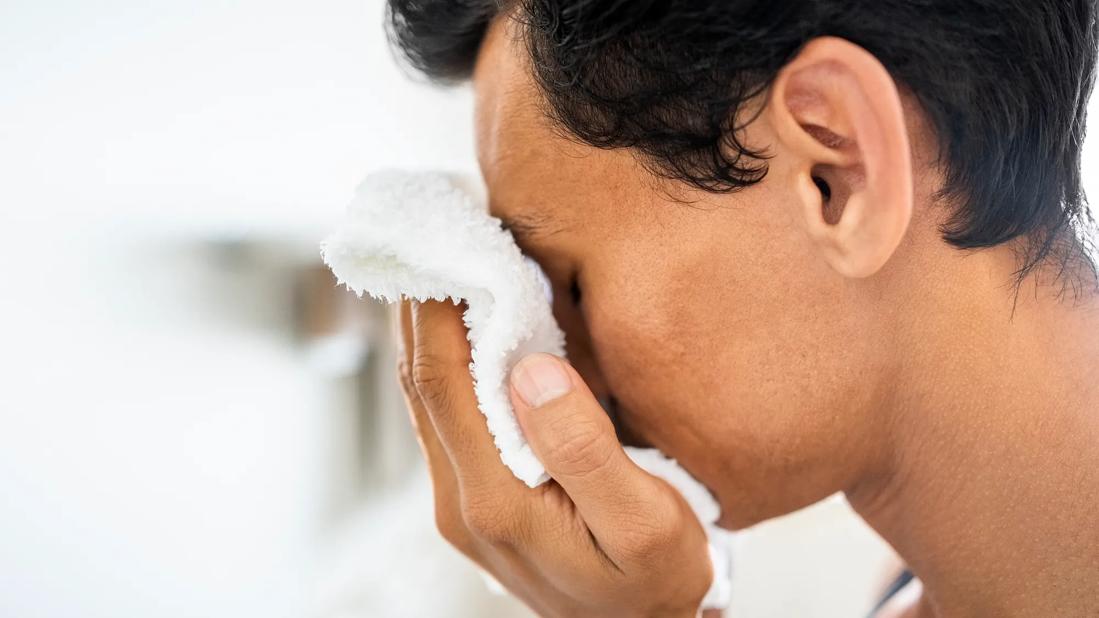 Person holding white washcloth to their face