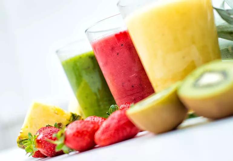 row of fruit slushies in glasses next to fruit