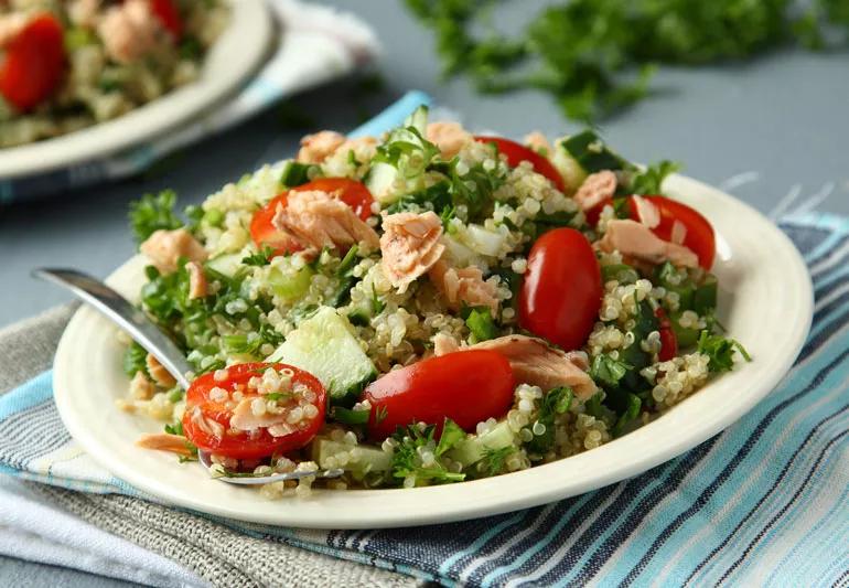 Toasted quinoa and salmon salad on a white plate, sitting on a colorful blue striped cloth napkin.