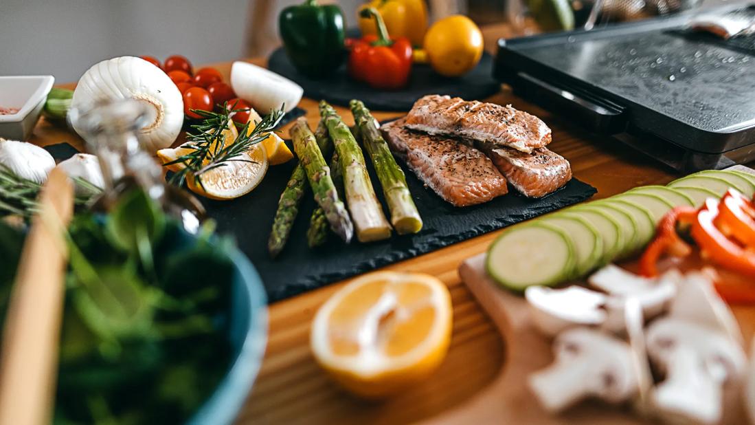 Table filled with fresh veggies and grilled asparagus and salmon