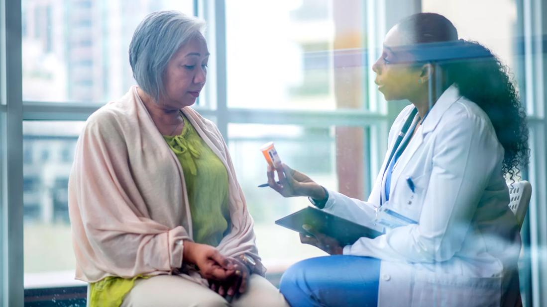 Healthcare provider holding prescription bottle talking with older female