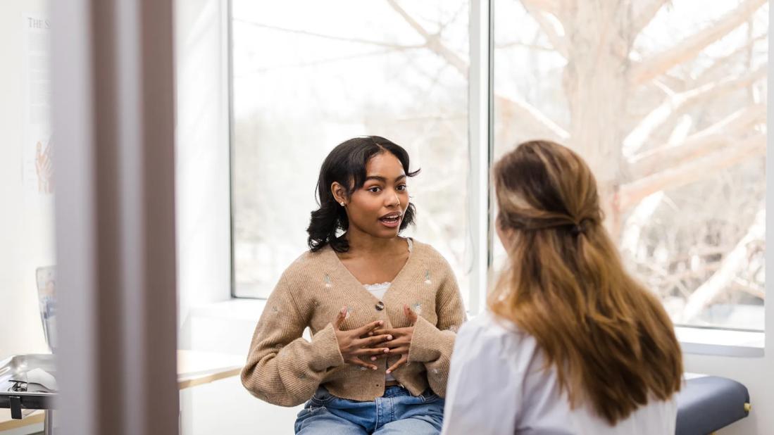 Teenager sitting on exam table talking to healthcare provider