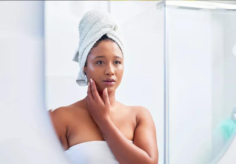 Person checking skin condition in bathroom mirror after a shower.