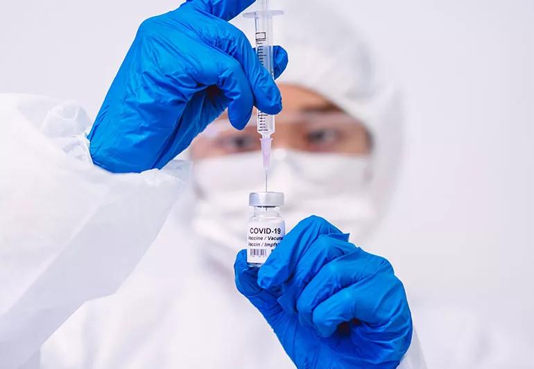 A healthcare provider uses a syringe to withdraw a COVID-19 vaccine from a small bottle.