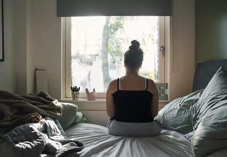 person sitting up in bed looking out the window