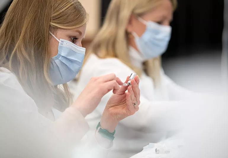 A healthcare provider uses a syringe to withdraw the COVID-19 vaccine from a small bottle.