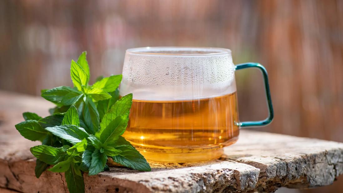 Cup of hot tea in glass mug, with peppermint sprigs near