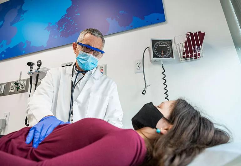 A healthcare provider checks on a patient's abdomen while the patient lays don on an examination table.