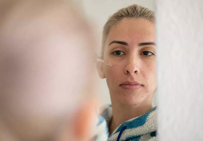 person putting tea tree oil on face in mirror