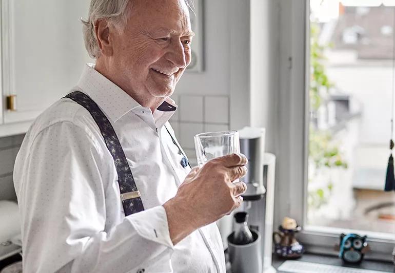 elderlay man drinks water in his kitchen
