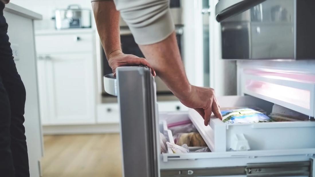 Arms of person bent down examining food in a bottom-of-fridge freezer bin