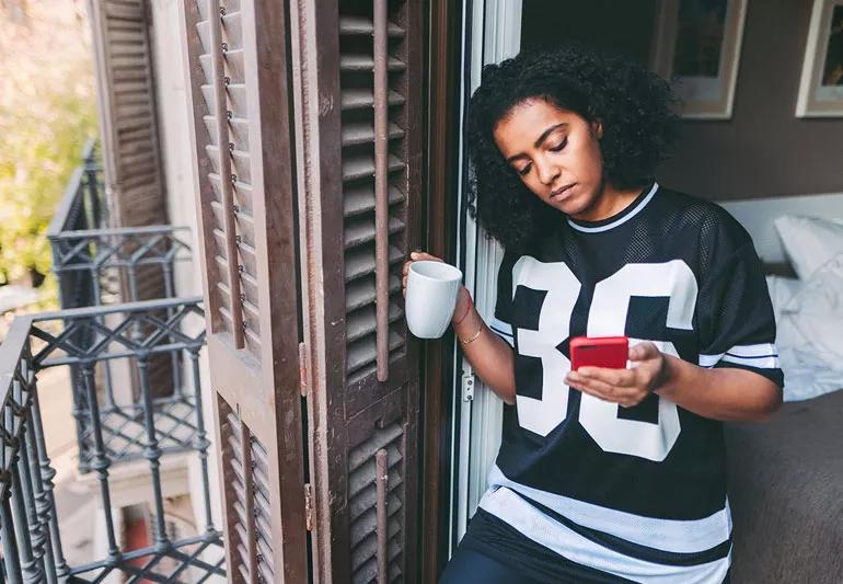Woman sheltering in place drinking coffee and checking phone while at home