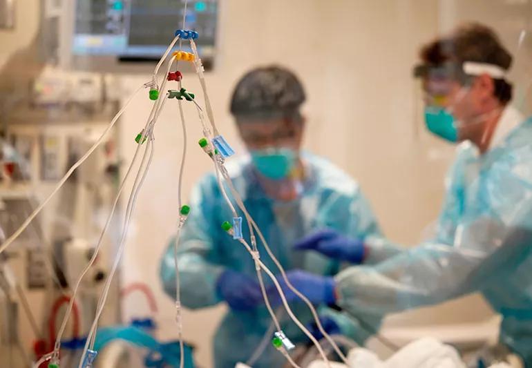 Two doctors in surgical masks treating a patient with COVID.