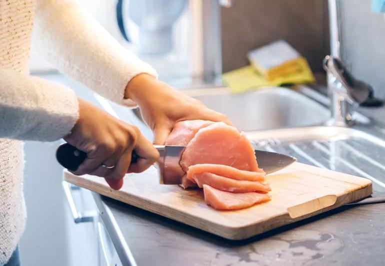 woman cutting raw meat on cutting board in kitchen