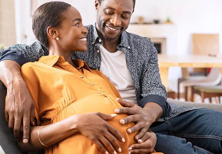 Man and pregnant partner at home on couch planning for baby.