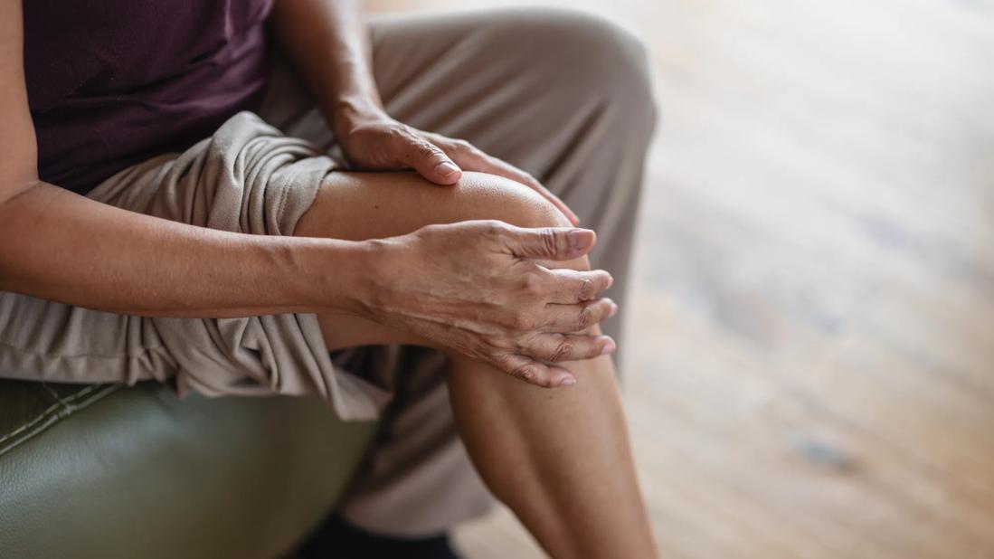 Person with pant leg pulled up, holding their knee with both hands