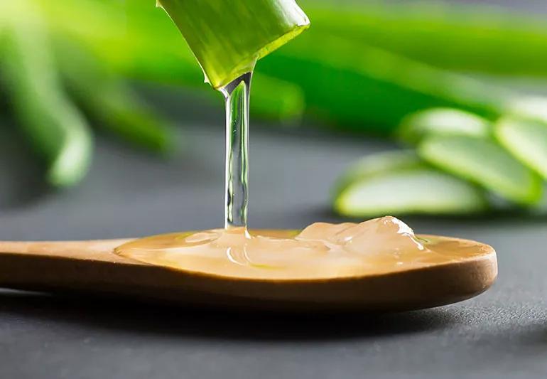 Aloe vera liquid being poured out of a plant onto a wooden board