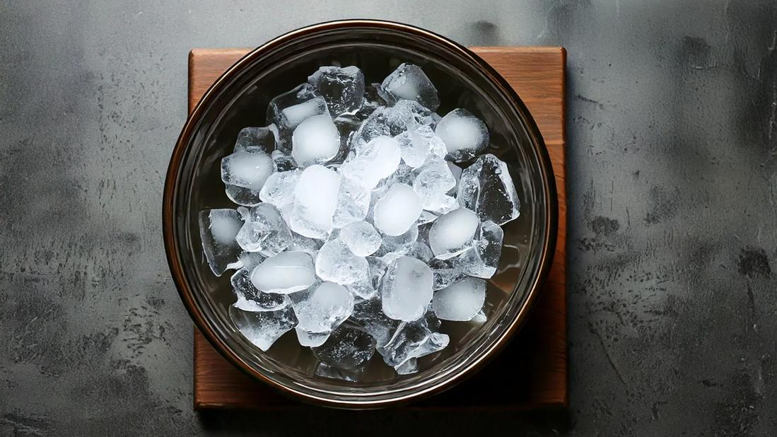 Metal bowl of icecubes on wooden block on table