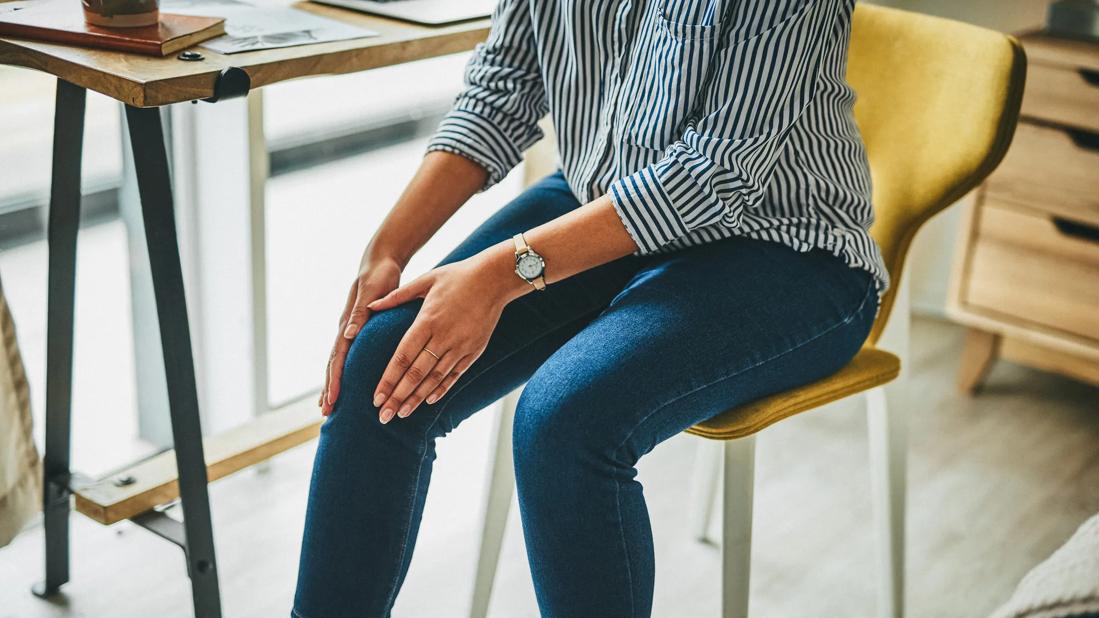 Person sitting at home desk chair rubbing their knee