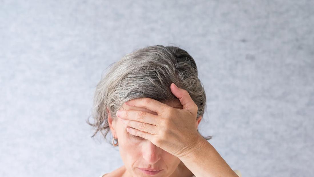 Older woman with gray hair with head bent down and hand on forehead, looking pensive