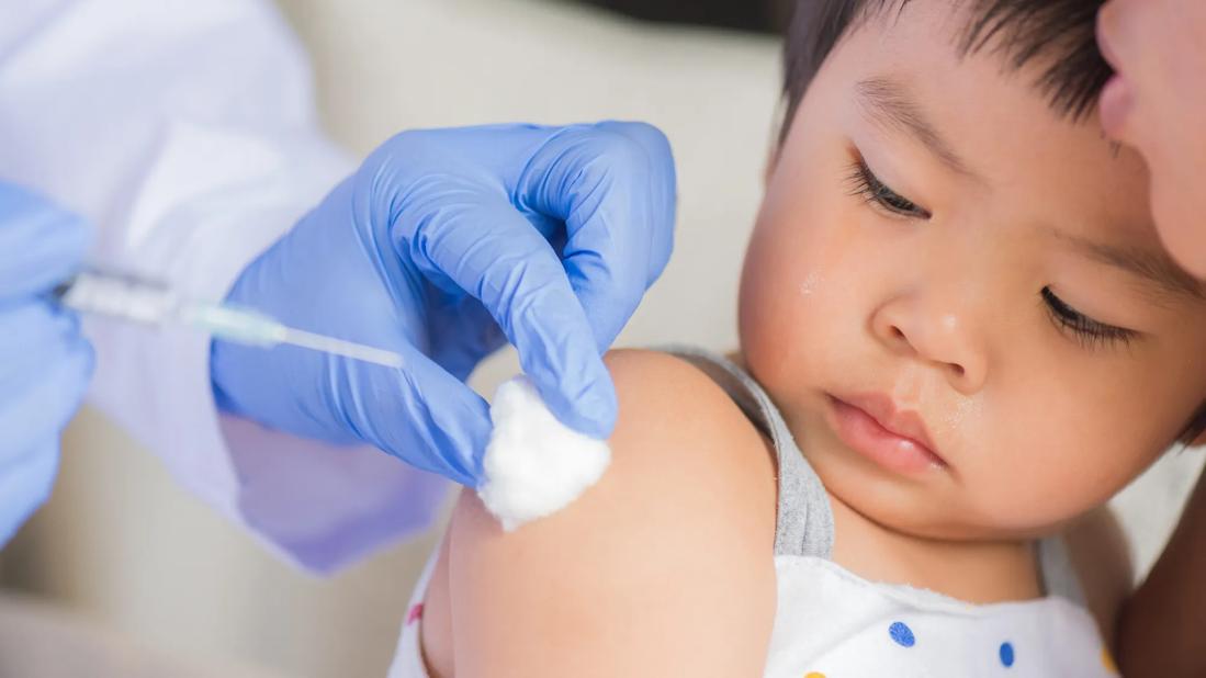 Gloved hands of healthcare provider giving a shot in the shoulder of a young child