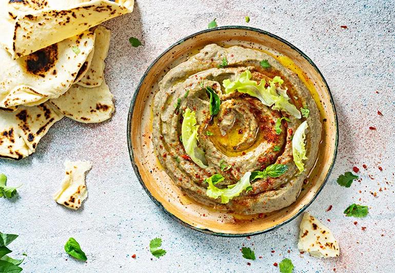 A bowl of baba ghanoush dip in a bowl with pieces of pita bread around it