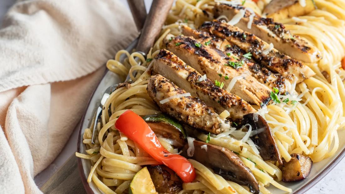 Platter of grilled chicken and vegetables over linguine