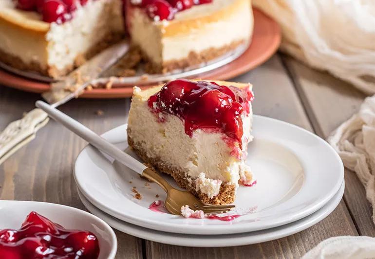 A slice of cheesecake with cherry topping on a plate next to a fork