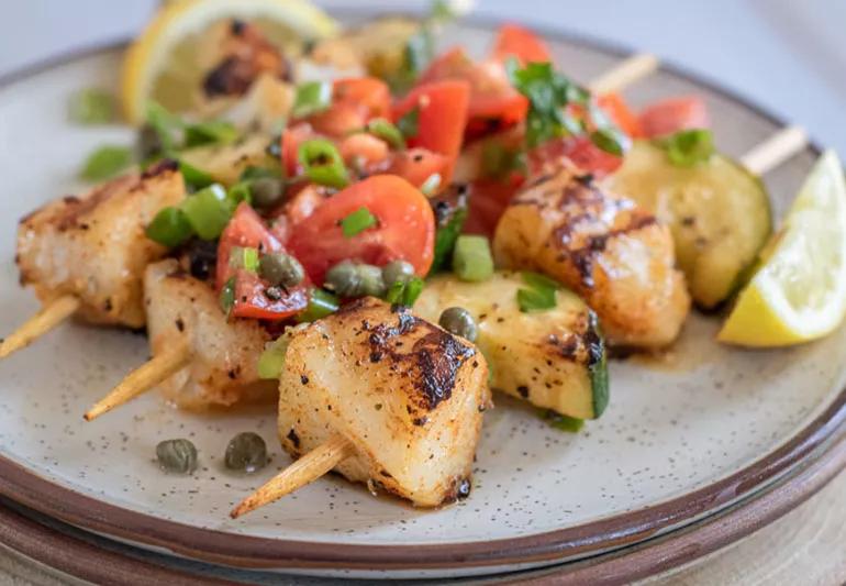 Fish kabobs on plate with lemon, tomato and capers