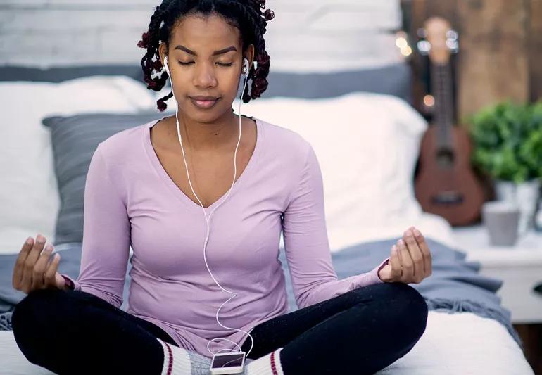 Teenager meditating and listening to music on bed